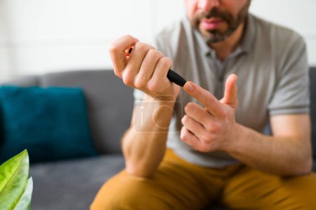 Téléchargez les photos : Gros plan d'un homme dans la trentaine diabétique vérifiant ses niveaux sanguins à l'aide d'un glucomètre dans son doigt - en image libre de droit