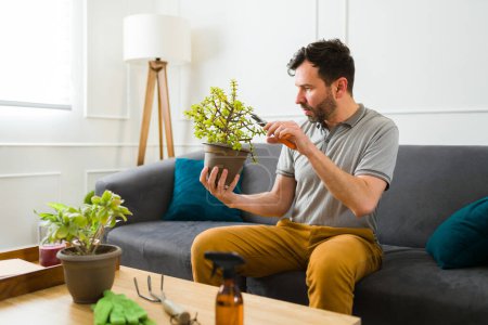 Foto de Hombre caucásico guapo disfrutando de su hobby de jardinería mientras cuida de sus plantas verdes en la sala de estar - Imagen libre de derechos