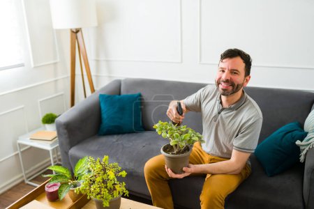 Photo for Portrait of a cheerful happy man making eye contact while enjoying gardening at home and watering his plants - Royalty Free Image