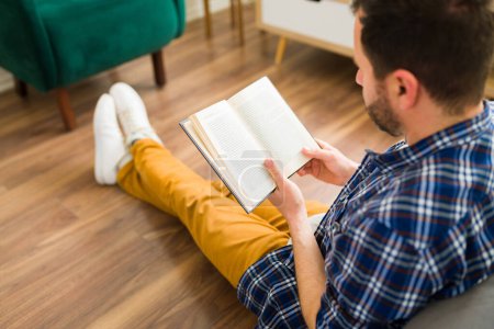 Téléchargez les photos : Homme caucasien dans sa trentaine vu de derrière tout en lisant un livre et se détendre à la maison pendant son temps libre - en image libre de droit