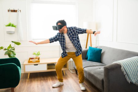 Foto de Divertido hombre caucásico de 30 años divirtiéndose jugando con gafas de realidad virtual durante un tiempo de ocio en casa - Imagen libre de derechos