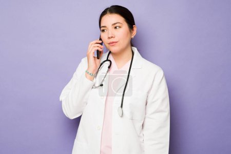Photo for Caucasian woman doctor using a white coat and a stethoscope talking on the phone with a patient - Royalty Free Image