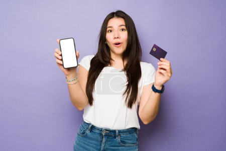Téléchargez les photos : Surprise jeune femme regardant excité et choqué tout en faisant des achats en ligne sur le smartphone payer avec une carte de crédit - en image libre de droit