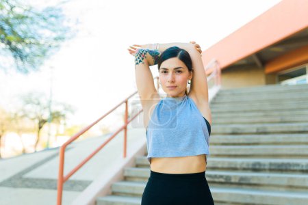 Photo for Portrait of a gorgeous active woman in her 20s stretching her arms above her head preparing for her workout exercises - Royalty Free Image