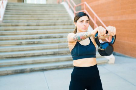 Photo for Beautiful fit young woman training outdoors using a kettlebell weight and exercising looking strong - Royalty Free Image