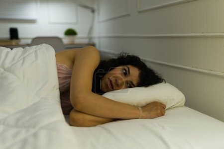 Téléchargez les photos : Belle femme hispanique regardant bouleversé tout en souffrant de problèmes de sommeil et d'insomnie tard dans la nuit dans sa chambre - en image libre de droit