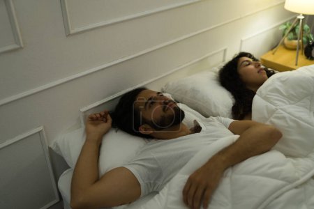 Téléchargez les photos : Jeune homme agité couché au lit à côté de son partenaire tout en ayant de l'insomnie et des problèmes de sommeil - en image libre de droit