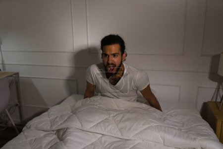 Photo for Scared hispanic man screaming feeling afraid after waking up from a scary nightmare in the middle of the night - Royalty Free Image