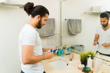 Foto de Hombre hispano poniendo pasta de dientes en un cepillo de dientes y preparándose para cepillarse los dientes en el baño por la mañana - Imagen libre de derechos