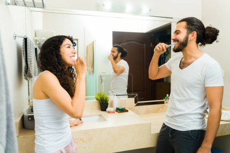 Foto de Emocionado mujer y hombre en pijama mirando en el amor en el baño mientras se cepillan los dientes - Imagen libre de derechos