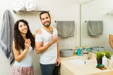 Téléchargez les photos : Couple latino attrayant souriant et utilisant un savon bio pour se laver pendant leur routine d'hygiène matinale dans la salle de bain - en image libre de droit