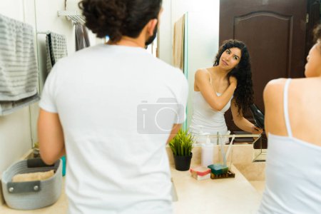 Téléchargez les photos : Beau couple avec des cheveux bouclés dans la salle de bain vu de derrière en utilisant des produits de toilettage et en faisant leur routine matinale - en image libre de droit