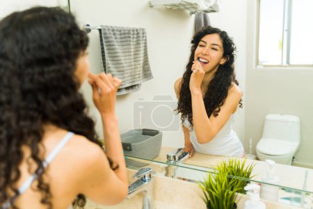 Foto de Joven mexicana con higiene dental cepillándose los dientes luciendo feliz mientras se prepara por la mañana - Imagen libre de derechos