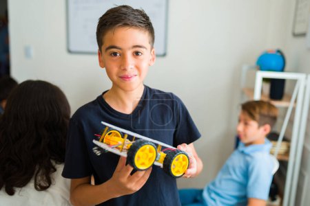 Portrait d'un jeune adolescent latino souriant établissant un contact visuel construisant un robot dans sa classe d'électronique au collège