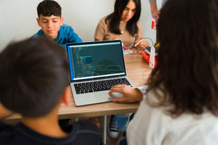 Photo for Hispanic teens seen from behind using a laptop computer while coding and programming robots during a group class - Royalty Free Image
