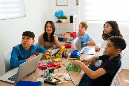 Foto de Niños y niñas felices prestando atención durante la clase mientras aprenden a codificar y construir robots o circuitos electrónicos - Imagen libre de derechos
