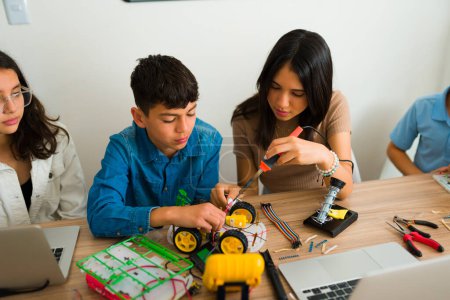 Téléchargez les photos : Jeunes garçons et filles intelligents adolescents travaillant ensemble à la construction d'un robot lors d'un projet collaboratif dans leur cours de robotique - en image libre de droit