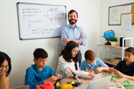 Photo for Happy proud teacher smiling looking cheerful for his smart teen students during an electronic or robotic class - Royalty Free Image