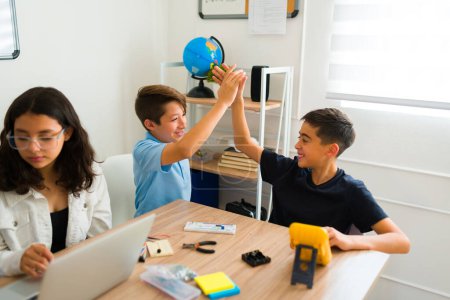 Téléchargez les photos : Jeunes garçons excités s'amusant à faire un high five après avoir fait un prototype de robot réussi ensemble sur un projet de robotique - en image libre de droit