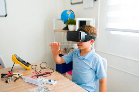 Téléchargez les photos : Adolescent caucasien garçon sourire tout en utilisant virtuel réalité lunettes avoir amusant lors de son robotique cours dans junior secondaire - en image libre de droit