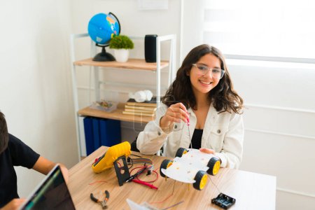 Téléchargez les photos : Joyeux jeune fille intelligente souriant regardant heureux tout en appréciant et en s'amusant pendant son cours de robotique - en image libre de droit