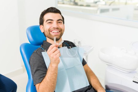 Foto de Alegre joven atractivo sonriendo mirando feliz con los resultados de su ortodoncia invisible en el dentista - Imagen libre de derechos