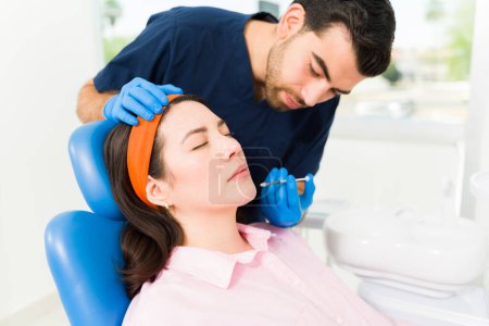 Foto de Médico varón haciendo un procedimiento de belleza en una mujer joven que recibe toxina botulínica o rellenos en el cuello o la cara - Imagen libre de derechos