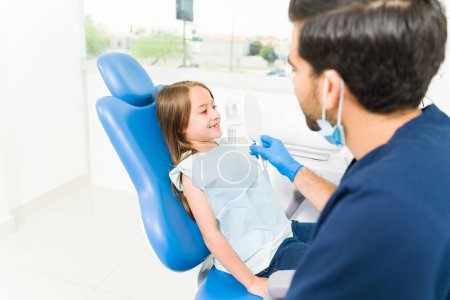 Téléchargez les photos : Adorable petite fille regardant ses dents blanches dans le miroir après un traitement des caries chez le dentiste pédiatre - en image libre de droit