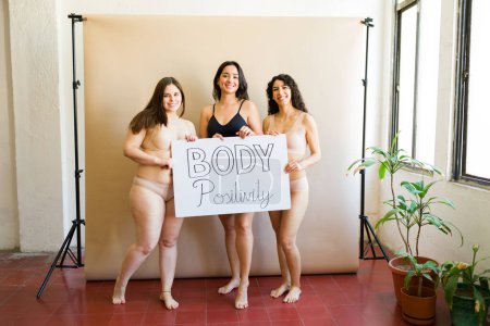 Foto de Tres amigas en ropa interior hermosa sosteniendo un cartel promoviendo la positividad corporal y la aceptación diversa debido al amor propio - Imagen libre de derechos