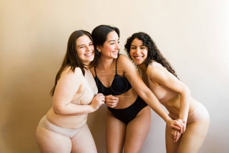 Foto de Mujeres caucásicas e hispanas con diversidad corporal usando ropa interior riéndose y divirtiéndose viéndose felices por el amor propio - Imagen libre de derechos