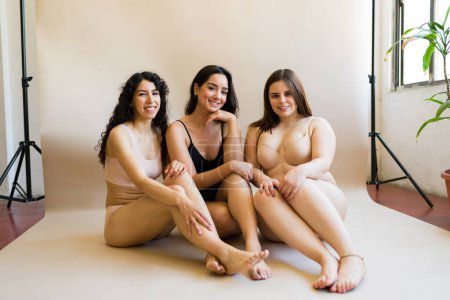 Téléchargez les photos : Magnifiques jeunes femmes avec la diversité du corps portant des sous-vêtements assis ensemble sentir beaucoup d'amour-propre - en image libre de droit