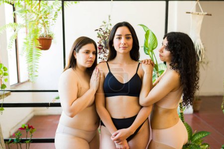 Foto de Atractivas mujeres morenas amorosas en ropa interior posando juntas promoviendo la diversidad corporal y la aceptación - Imagen libre de derechos