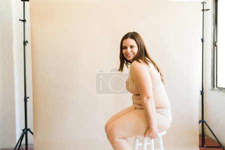Téléchargez les photos : Vue latérale d'une femme caucasienne heureuse plus la taille relaxant dans ses sous-vêtements souriant heureux sur la diversité du corps - en image libre de droit