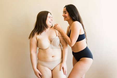 Téléchargez les photos : Meilleures amies gaies riant et s'amusant tout en parlant d'amour de soi et d'acceptation du corps portant des sous-vêtements - en image libre de droit