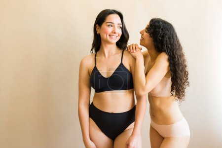Foto de Emocionados mejores amigos femeninos hablando de amor propio y positividad corporal mientras usan ropa interior hermosa - Imagen libre de derechos
