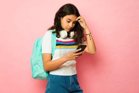 Téléchargez les photos : Inquiète adolescente va à l'école et reçoit de mauvaises nouvelles tout en envoyant des SMS sur son smartphone à la recherche bouleversée - en image libre de droit