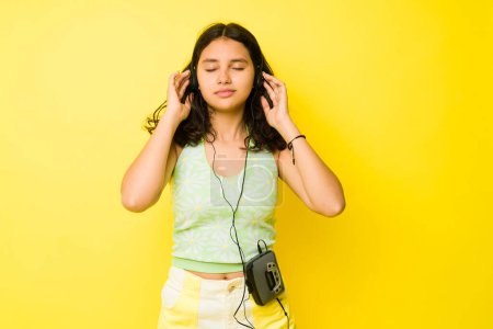 Photo for Latin adorable teen girl putting on retro headphones and listening to vintage music while looking relaxed - Royalty Free Image