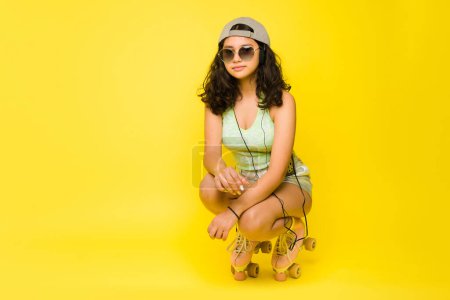 Photo for Hispanic teen girl having fun roller skating using vintage roller skates and summer sunglasses next to yellow copy space - Royalty Free Image