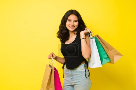 Téléchargez les photos : Adorable adolescente hispanique faisant du shopping au centre commercial et portant beaucoup de sacs et regardant heureux - en image libre de droit