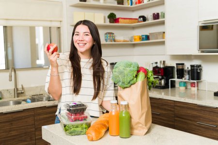 Photo for Excited beautiful woman with a vegan lifestyle looking cheerful while ready to cook with healthy vegetables and fruit in the kitchen - Royalty Free Image