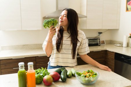 Téléchargez les photos : Femme végétarienne détendue appréciant le mode de vie végétalien et prête à cuisiner des aliments sains avec des légumes biologiques dans la cuisine - en image libre de droit