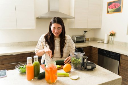 Foto de Mujer vegetariana caucásica cortando verduras orgánicas en la cocina y preparando jugos verdes y batidos de frutas - Imagen libre de derechos