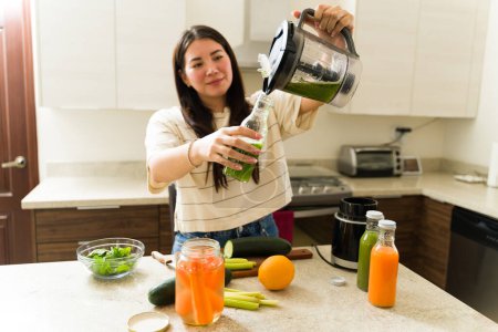 Photo for Excited healthy woman with a vegetarian lifestyle preparing a green juice or smoothie in her blender - Royalty Free Image