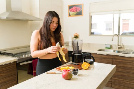Photo for Active caucasian woman preparing a fruit smoothie in the blender while having a vegan healthy lifestyle after exercising - Royalty Free Image
