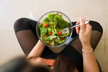 Photo for Top view of a fit woman with a healthy vegetarian lifestyle eating a green organic salad after exercise - Royalty Free Image