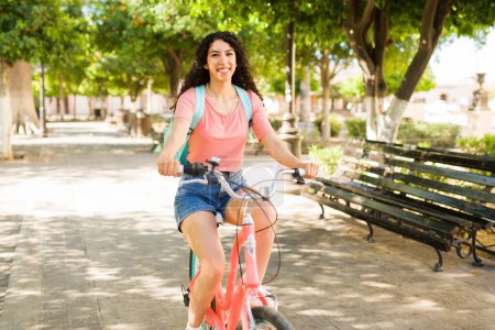 Téléchargez les photos : Femme hispanique joyeuse s'amuser à vélo et s'amuser dans le parc pendant son trajet en plein air en été - en image libre de droit