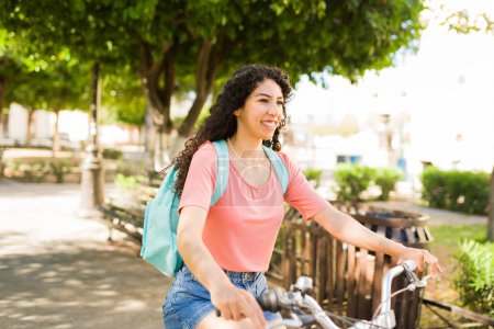 Téléchargez les photos : Une jeune femme souriante et joyeuse qui part en balade à vélo et se promène dans le parc par une belle journée d'été - en image libre de droit