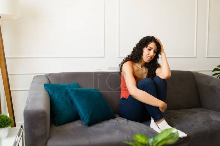Photo for Lonely young woman feeling sad and depressed while suffering from anxiety sitting on the sofa at home - Royalty Free Image