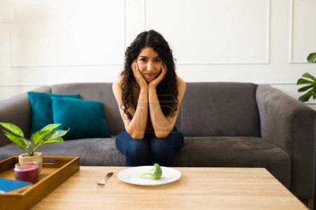 Photo for Sick young woman making eye contact while trying to eat and suffering from eating problems alone at home - Royalty Free Image