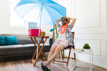 Photo for Relaxed happy man smiling relaxing in a beach chair and parasol at home wearing shorts during the summer vacation at home - Royalty Free Image